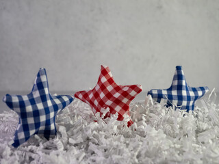 Red white and blue checker fabric covered stars standing up on a bed of white paper shreds with a plaster background.  Perfect for 4th of July, Veteran’s Day, Memorial Day and patriotism.