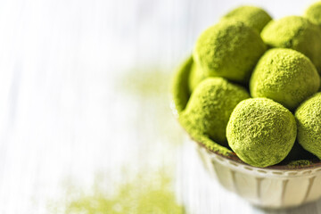 Homemade truffle sweets with green matcha tea in a ceramic bowl on a light wooden background. Raw...