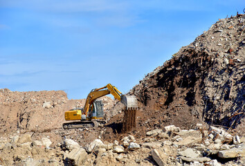 Yellow excavator at landfill for disposal of construction waste. Backhoe dig gravel at mining...