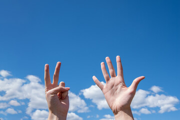 Close-up of female hands showing seven fingers on a blue sky background. Number seven in sign language. Copy space
