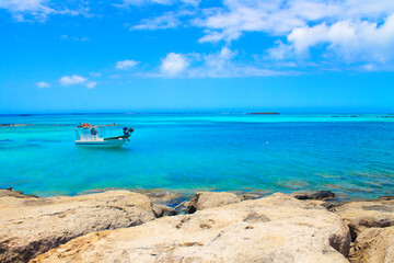 Obraz premium Greece. Crete. 22.06.2020. View of small fish boat, stones, turquoise water and clouds in blue sky.