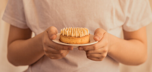Child holds a plate with vanilla tart and cream in a soft light.