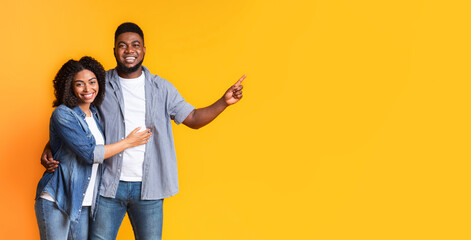 Positive Black Spouses Cuddling and Pointing At Copy Space On Yellow Background