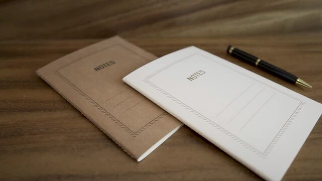 Libro de notas blanco y caf&eacute; con bol&iacute;grafo.