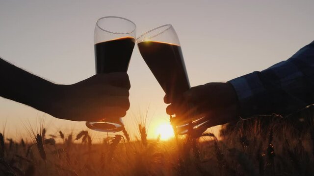 Hands with glasses of beer clink glasses on the background of a field of wheat