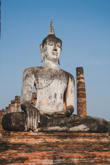 Fototapeta na wymiar The large old Buddha statue Enshrined stands majestically in the Sukhothai Historical Park. Amid the orange-coloured sky during the evening, Sukhothai Province, Thailand