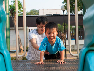 Asian child boy playing in playground together with dad in happy family time. Father support son with love and care.