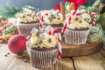 Christmas cupcakes. Xmas hot chocolate cupcake with peppermint candy cane, chocolate drops and marshmallow. Wooden background with Christmas decor and fir tree branches. Sweet Christmas baking/