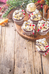 Christmas cupcakes. Xmas hot chocolate cupcake with peppermint candy cane, chocolate drops and marshmallow. Wooden background with Christmas decor and fir tree branches. Sweet Christmas baking/