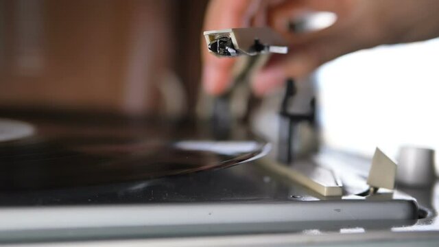 woman hand puts needle onto black vinyl plate on vintage record player turntable to listen music on blurred background extreme close view