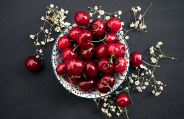 A bowl full of cherries in the center of a dark background. View from above