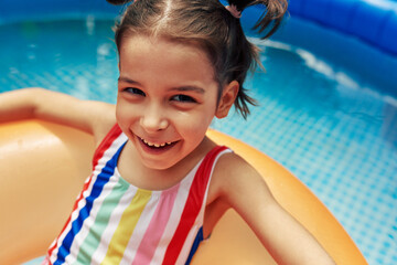 Closeup portrait of smiling kid wears colorful swimsuit relaxing on an inflatable ring floating in...