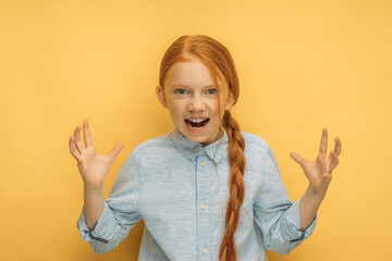 angry, playful and scary child girl is teasing on the yellow studio background and looking at...