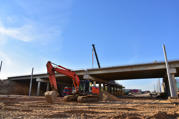 Excavator working at construction highway ramps and bridgeworks. Roundabout and traffic bridge construction. Road work on traffic highway, road intersection junction and freeway. Bridge project works