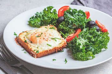 Baked egg and cheese toast with salad on a white plate, close-up.