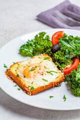 Baked egg with cheese toast with salad on a white plate.