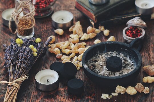 Many little pieces of light yellow Yemen frankincense resin incense on dark wooden table. Charcoal disk in black holder ready for air cleansing ceremony on a busy and cluttered wiccan witch altar