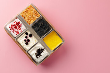 Mousse desserts in square plastic boxes with different toppings on pink table