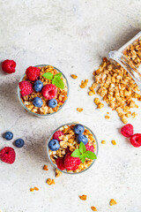 Obraz na płótnie Canvas Yogurt parfait with granola, raspberries and blueberries in glasses, light gray background, top view. Healthy breakfast concept.