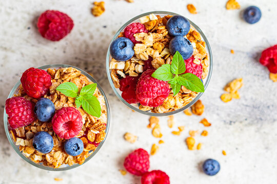 Yogurt parfait with granola, raspberries and blueberries in glasses, light gray background, top view. Healthy breakfast concept.
