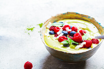 Matcha tea green smoothie bowl with berries and coconut, gray background. Healthy vegan food concept.
