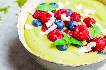 Matcha tea green smoothie bowl with berries and coconut, close-up, gray background. Healthy vegan food concept.