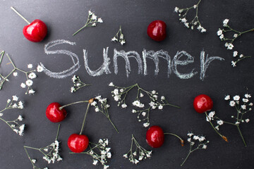 Inscription summer on a blackboard
written with white chalk. Board decorated with red cherries and white small flowers