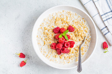 Breakfast oatmeal with raspberries in a white bowl, top view. Healthy breakfast concept.