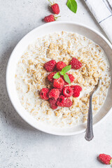 Breakfast oatmeal with raspberries in a white bowl, top view. Healthy breakfast concept.