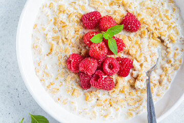 Breakfast oatmeal with raspberries in a white bowl, top view. Healthy breakfast concept.