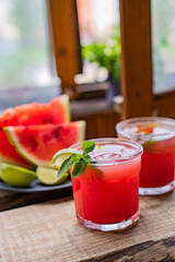 Watermelon smoothie lemonade with lime, topping with fresh mint leaves for the summer drinks concept. Homemade refreshing cold drink on wooden rustic table near window. Selective focus, copy space.