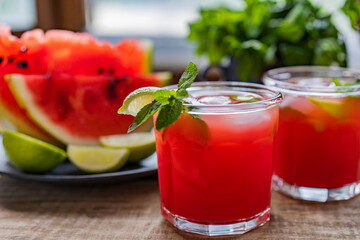 Watermelon smoothie lemonade with lime, topping with fresh mint leaves for the summer drinks concept. Homemade refreshing cold drink on wooden rustic table near window. Selective focus, copy space.