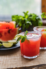 Watermelon smoothie lemonade with lime, topping with fresh mint leaves for the summer drinks concept. Homemade refreshing cold drink on wooden rustic table near window. Selective focus, copy space.