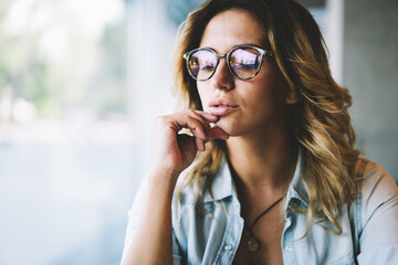 Clever pondering hipster girl in optical spectacles for provide eyes protection feeling confused on information during leisure time, caucasian contemplative woman in eyewear thinking about ideas