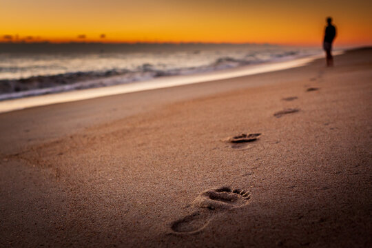 A person walking on the beach leaving footprints in the sand - Powered by Adobe