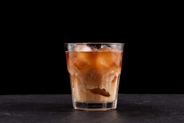 Iced coffee in a tall glass with cream poured over. Dark background, copy space