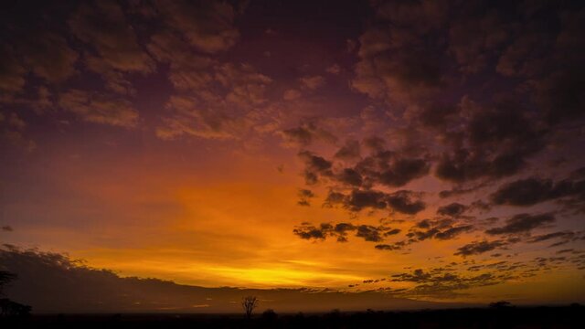 Stunning sunrise timelapse over African plains with mountains and red sky, clouds illuminated
