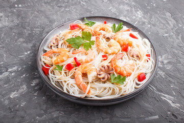 Rice noodles with shrimps or prawns and small octopuses on gray ceramic plate on a black concrete background. Side view.