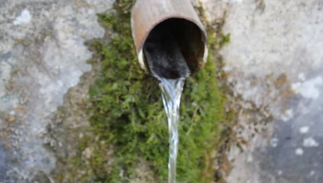 Near a fountain where spring water from a natural source flows through a pipe or spout