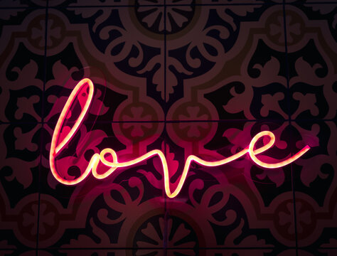Love. Neon sign letter word Love in bright red colours glow in the dark on pattern tiles wall background.