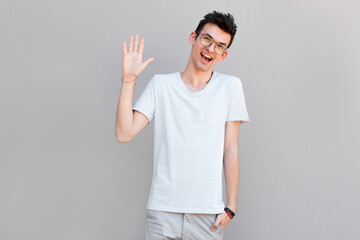 Friendly positive smiling bearded man in grey t-shirt waving with his hand, hailing business...