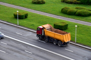 Dump truck carries sand along a road in a city. View from above. Object in motion, soft focus, possible graininess © MaxSafaniuk