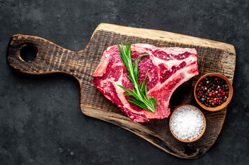 Raw cowboy steak. Marbled beef meat 
with spices on a stone background