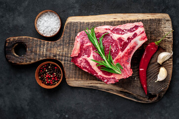 Raw cowboy steak. Marbled beef meat 
with spices on a stone background