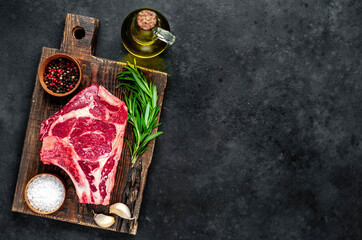 Raw cowboy steak. Marbled beef meat with spices on a stone background