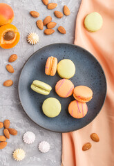 Orange and green macarons or macaroons cakes on blue ceramic plate on a gray concrete background. top view, close up.