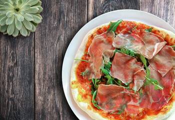 above view of fresh homemade delicious italian pizza with Serrano ham and arugula on rustic wooden table