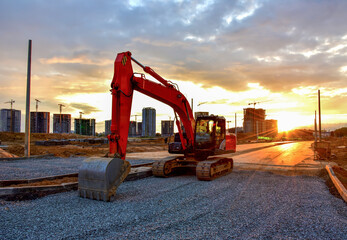 Excavator during road work at construction site on awesome sunset background. Screeding gravel for...