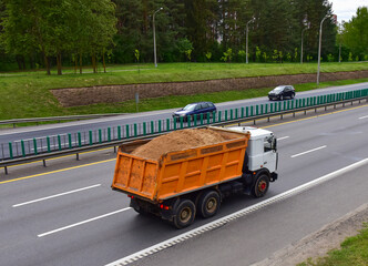 Dump truck transports sand along a road in a city. Object in motion, soft focus, possible graininess © MaxSafaniuk