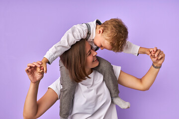 playful little caucasian boy hugs her mother neck and looks at her with a smile, parent and chil in love, happy